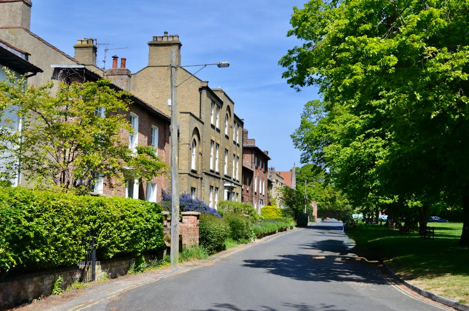 A quiet residential street on a cloudy day in Fortess Road, Tufnell Park, featuring a row of Victorian-style terraced houses with white facades, bay windows, and red-tiled roofs. The pavement is clean